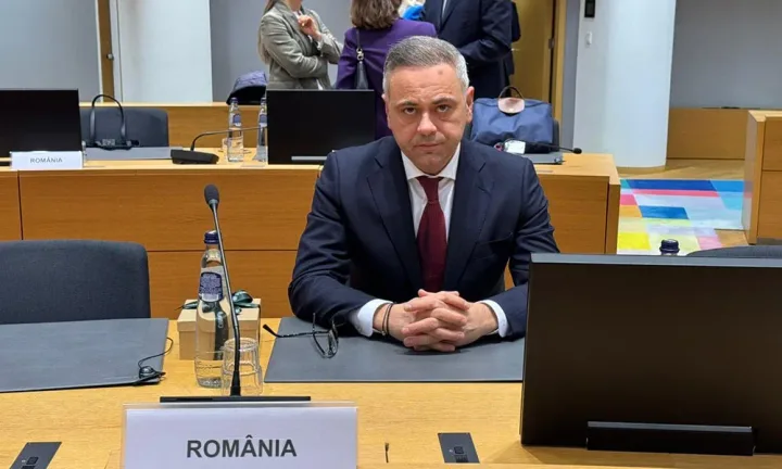 Un bărbat îmbrăcat elegant stă la o masă într-o sală de conferințe.