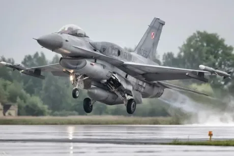 Avion de luptă decolând pe un aeroport militar, pe fundal verde.