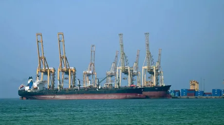 Vapor de marfă ancorat în port, cu macarale în fundal.
