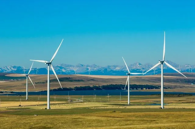 Turbine eoliene amplasate pe un peisaj natural vast, sub un cer senin.