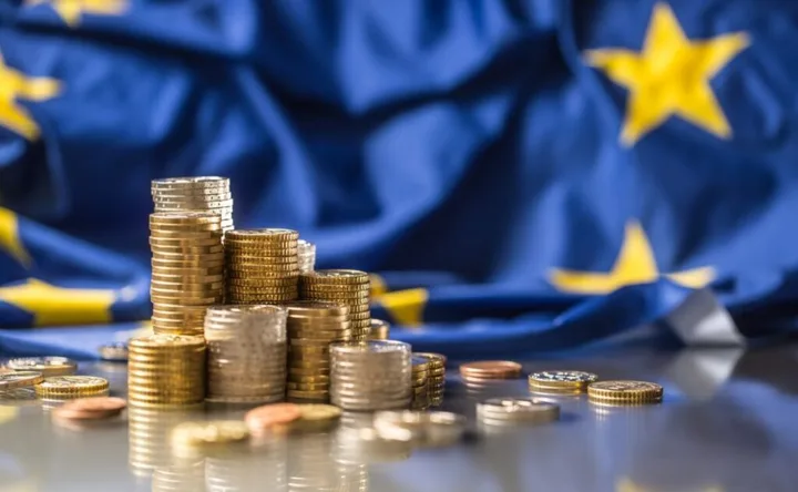 Monede aranjate pe un fundal cu steagul Uniunii Europene.