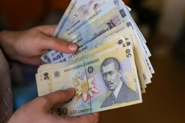 Bancnote românești în mână, simbolizând salariile și inflația.