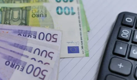 Bancnote de euro pe un birou, alături de un calculator.