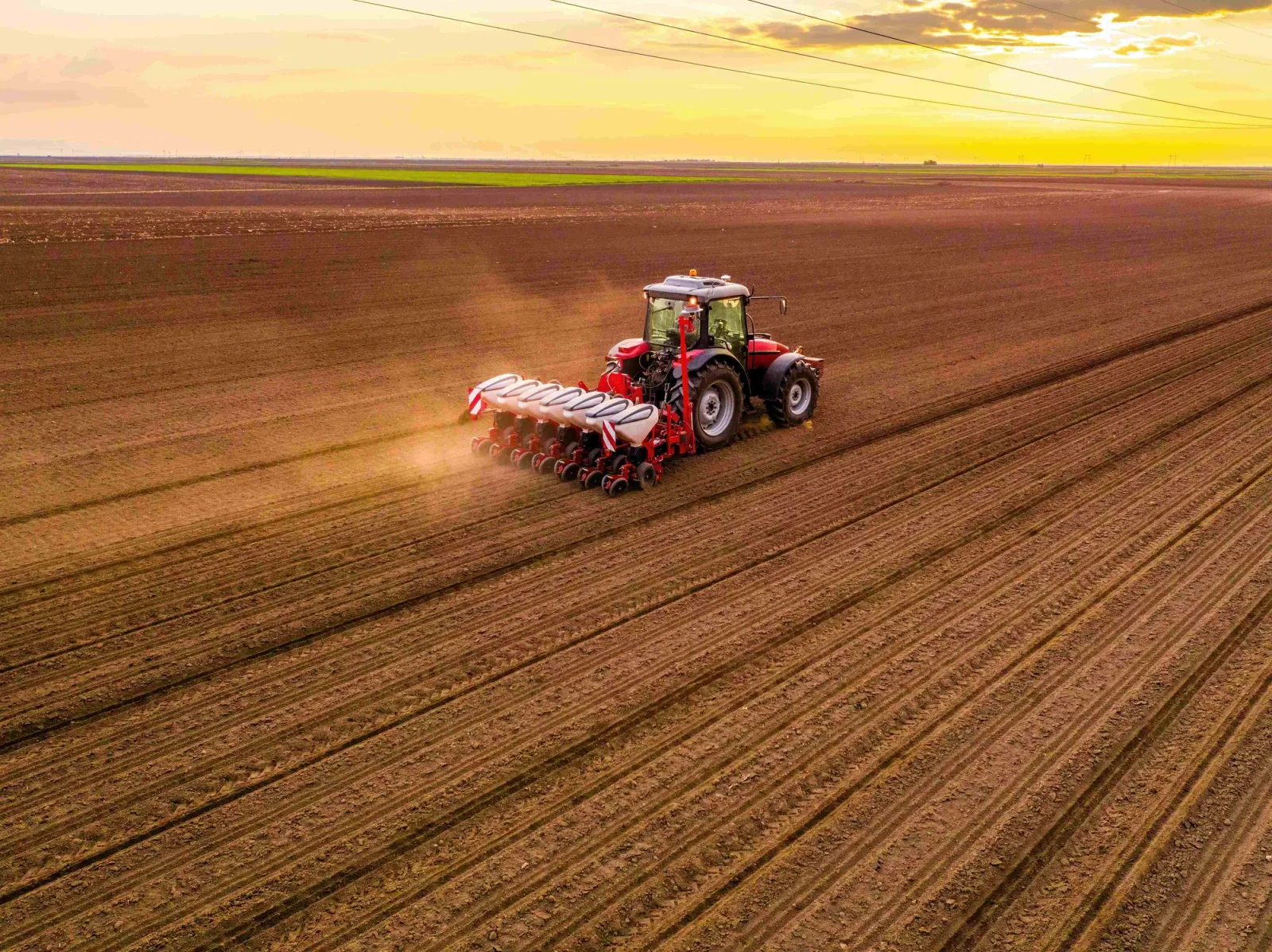 Tractor semănând pe un câmp vast la apus.