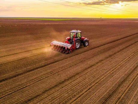 Tractor semănând pe un câmp vast la apus.
