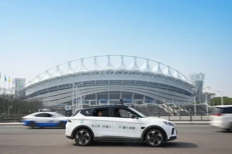 Un robotaxi circulând pe stradă, cu un stadion în fundal.