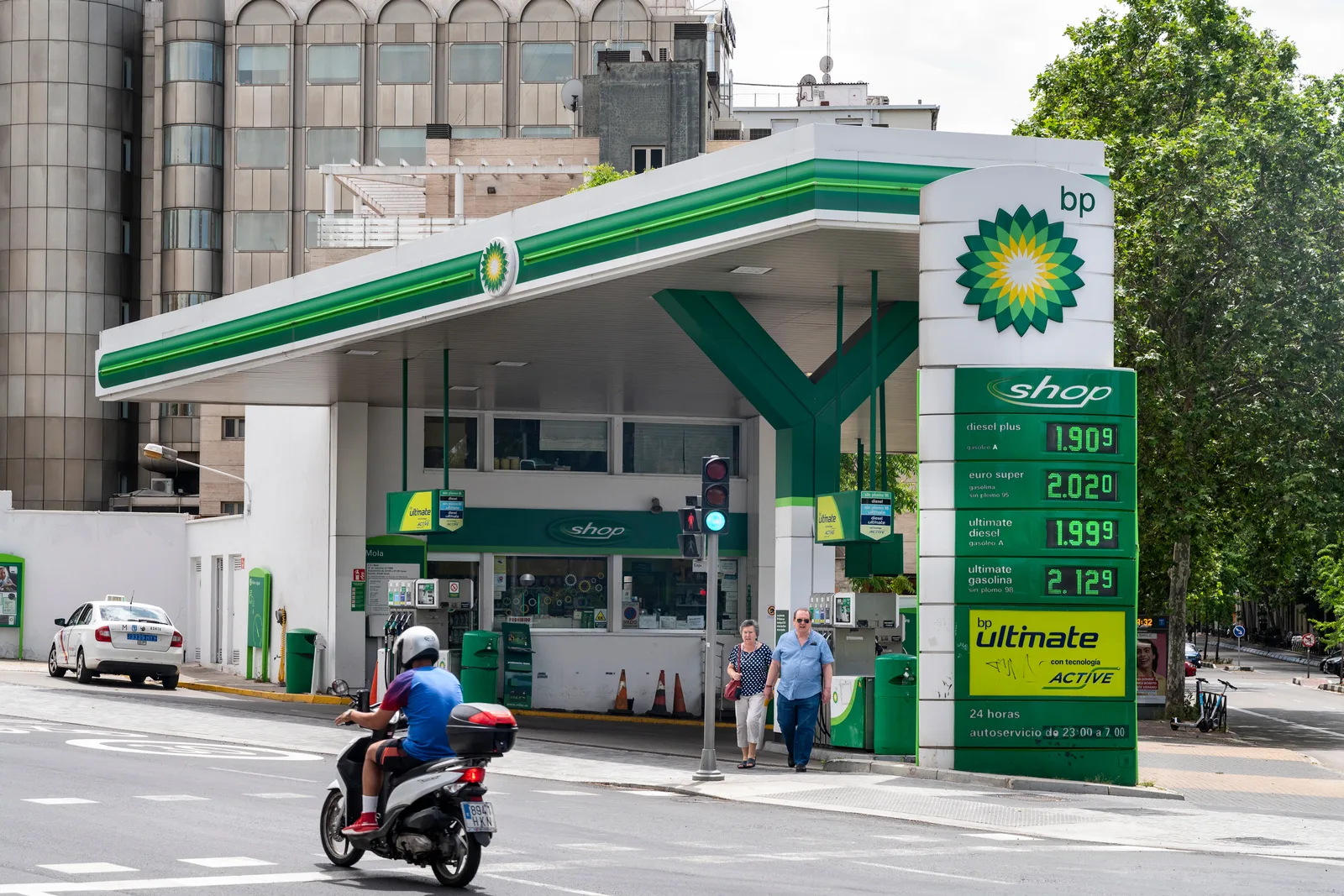 Stație de benzină BP cu prețuri afișate și clienți la cumpărături.