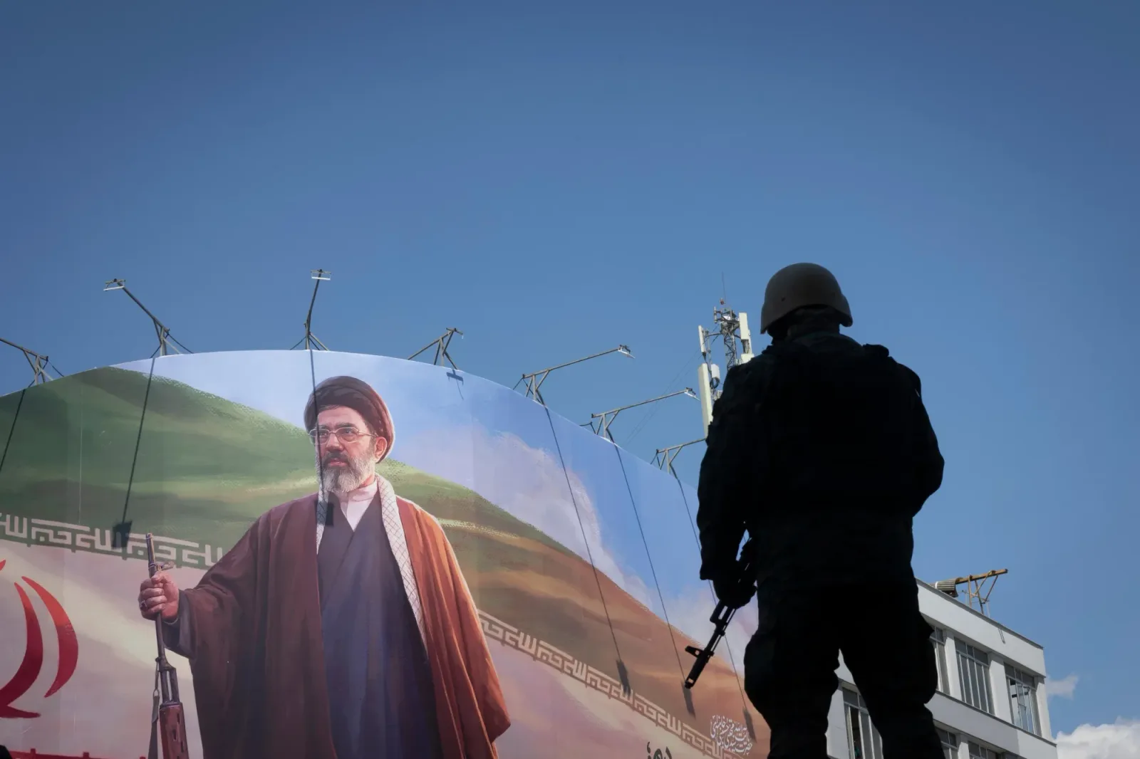 Un soldat privește un mural cu un lider iranian în fundal.