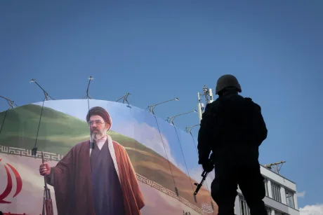 Un soldat privește un mural cu un lider iranian în fundal.