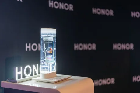 Un smartphone expus pe un suport iluminat, cu logo-ul Honor în fundal.