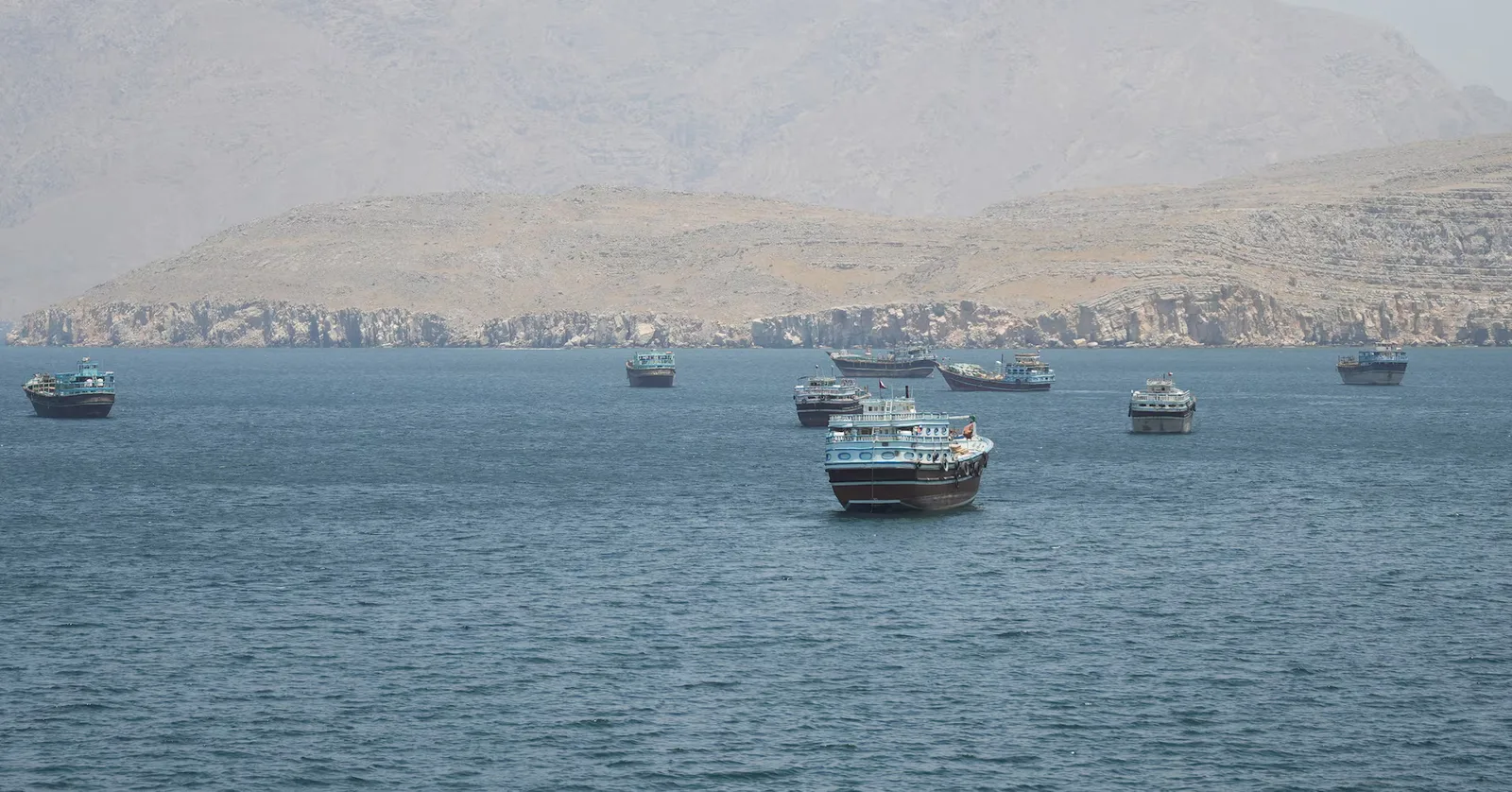 Vaporase ancorate în Strâmtoarea Hormuz, pe fundal montan.
