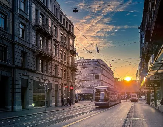 Peisaj urban din Elveția la apus, cu tramvaie și clădiri istorice.