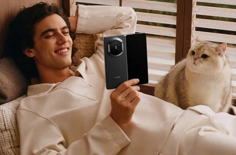 Un tânăr relaxat, folosind un telefon pliabil, alături de o pisică pe canapea.