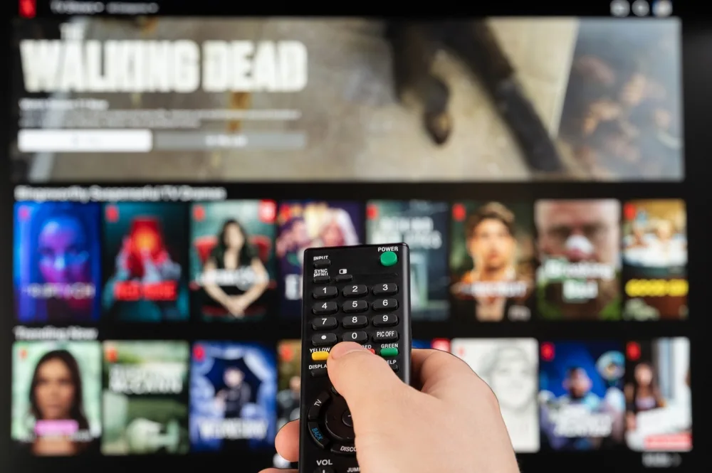 Un telecomandă îndreptată spre un ecran cu filme și seriale.