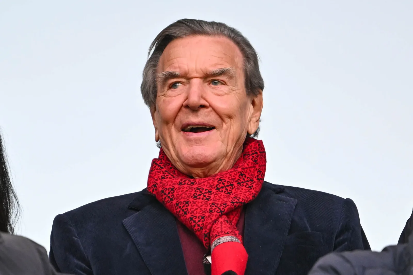 Gerhard Schröder zâmbind, purtând o eșarfă roșie, în context politic german.