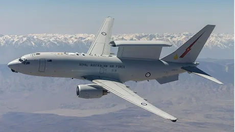 Aeronava Boeing E-7A în zbor, cu peisaj montan în fundal.
