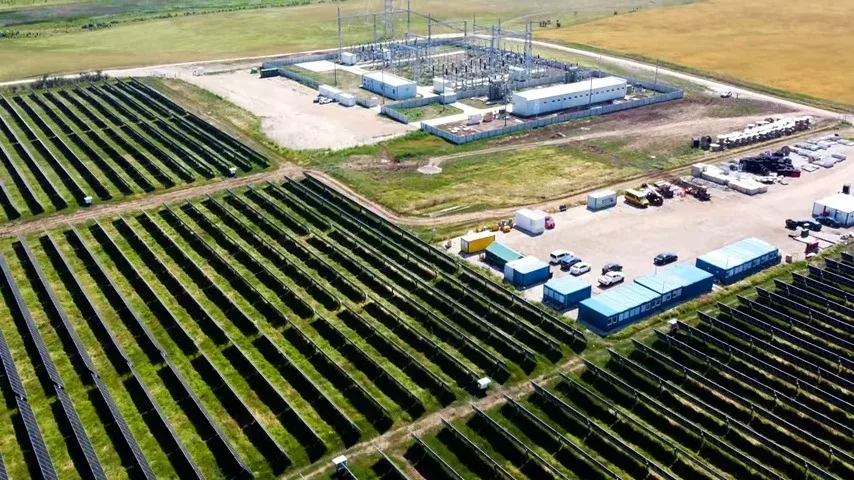 Panouri solare amplasate pe teren agricol, cu stație electrică în fundal.