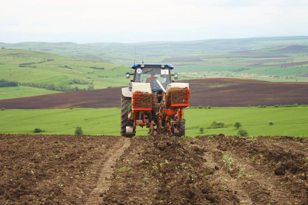 Tractor lucrând pe un câmp verde, pregătind solul pentru cultivare.