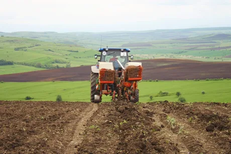 Tractor lucrând pe un câmp verde, pregătind solul pentru cultivare.