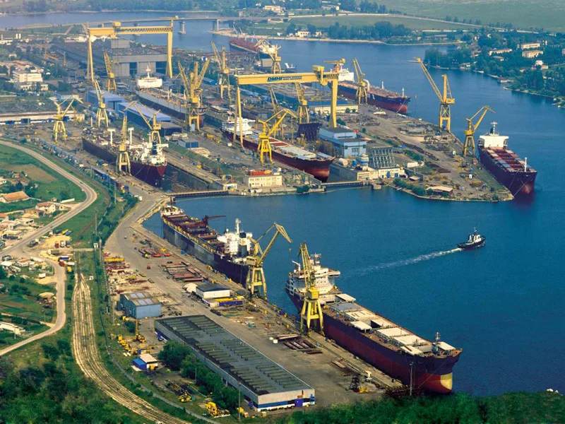 Vedere aeriană a șantierului naval Damen Shipyards din Mangalia, cu nave și echipamente pe apă.