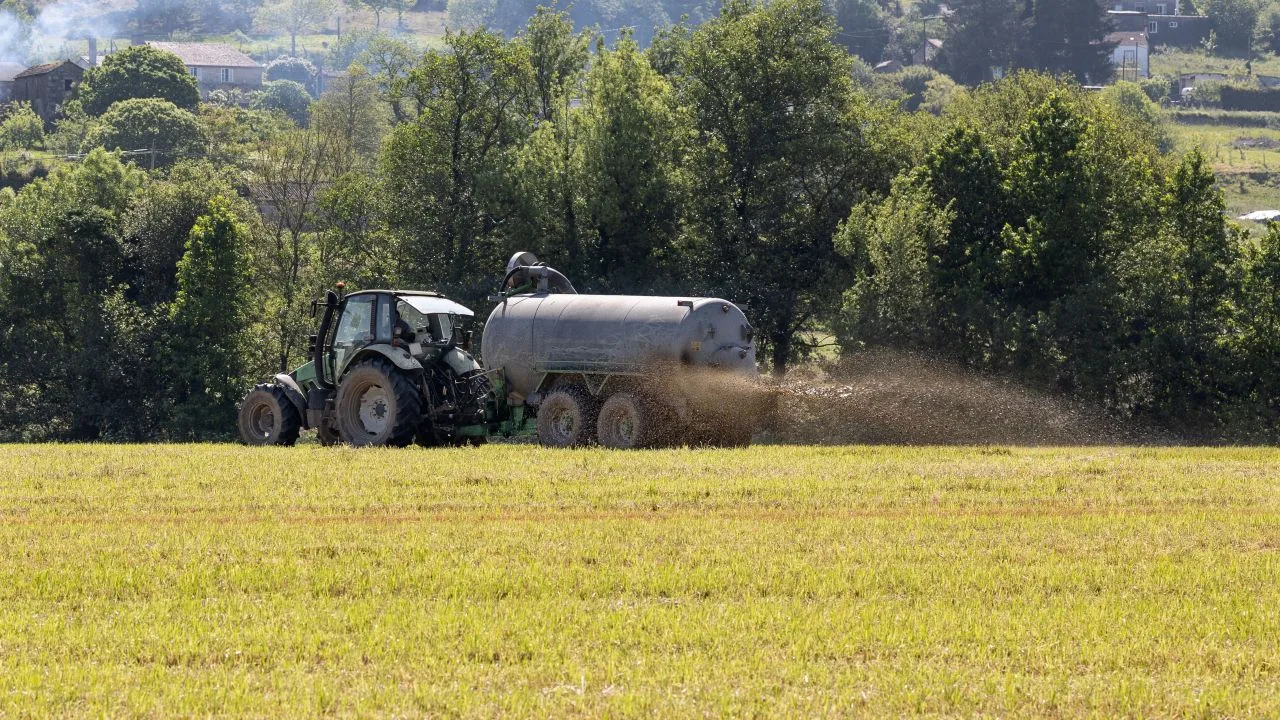 Tractor aplicând gunoi de grajd lichid pe un câmp verde.