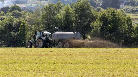 Tractor aplicând gunoi de grajd lichid pe un câmp verde.