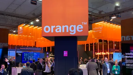 Standul Orange la un eveniment tehnologic, cu mulți participanți și iluminare vibrantă.