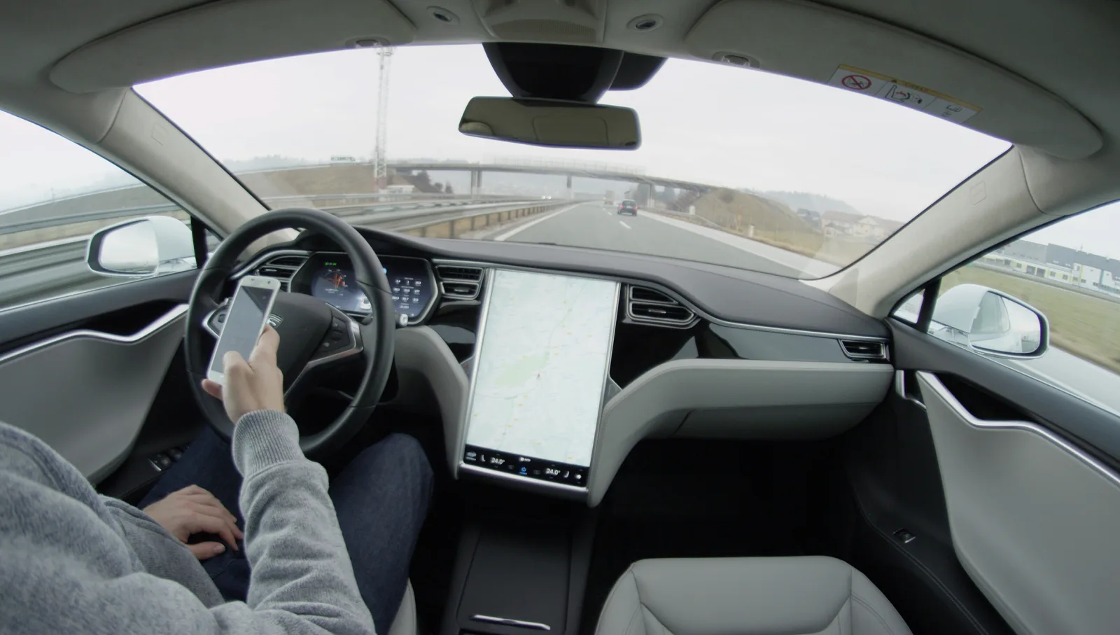 Mașină Tesla pe autostradă, cu conducere autonomă activată și supraveghere umană.