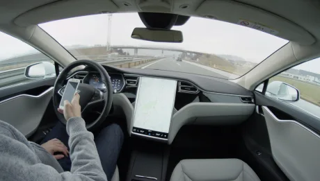 Mașină Tesla pe autostradă, cu conducere autonomă activată și supraveghere umană.