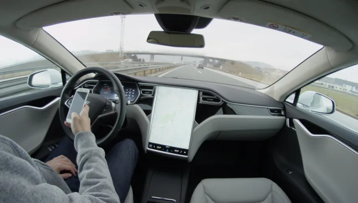Mașină Tesla pe autostradă, cu conducere autonomă activată și supraveghere umană.