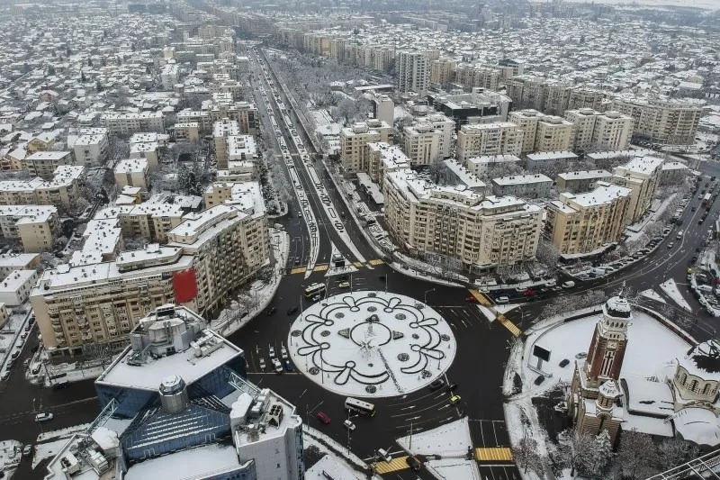 Peisaj urban acoperit de zăpadă, clădiri moderne și circulație intensă.