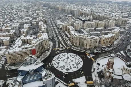 Peisaj urban acoperit de zăpadă, clădiri moderne și circulație intensă.