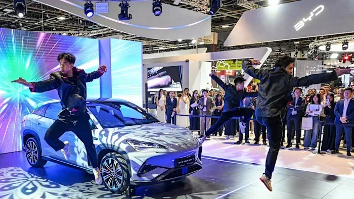 Spectacol de dans la un eveniment auto din China, cu un vehicul electric în fundal.