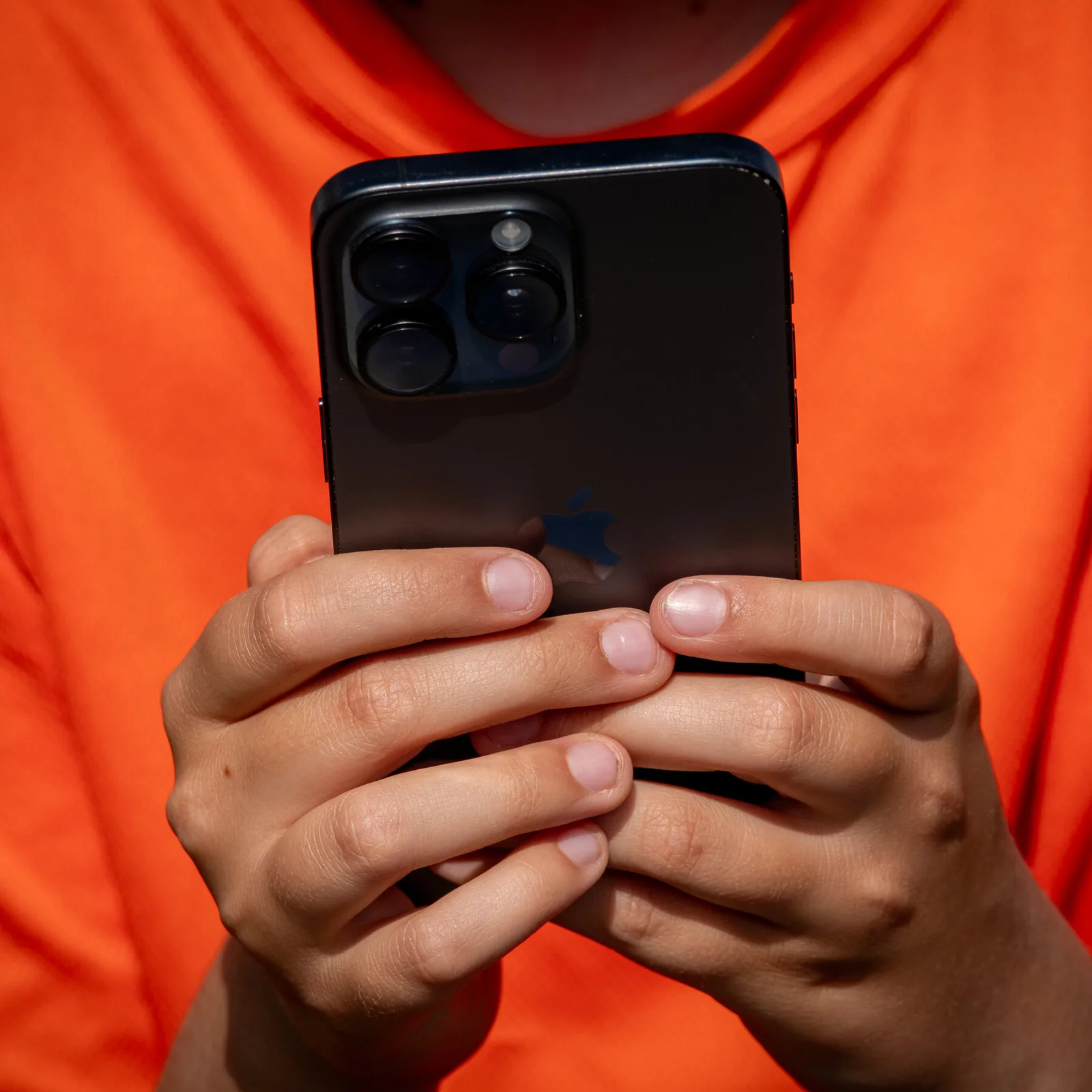 Un tânăr ținând un telefon mobil în mână, concentrat pe ecran.