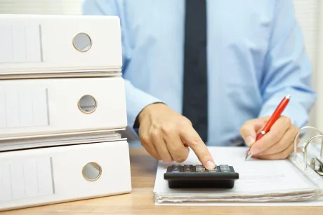 Persoană care completează documente financiare și folosește un calculator.