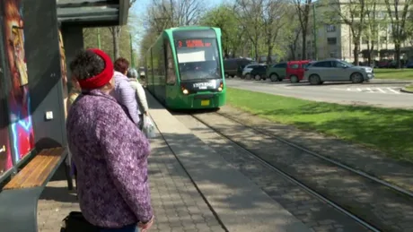 Oameni așteptând tramvaiul pe o stradă dintr-un oraș românesc.