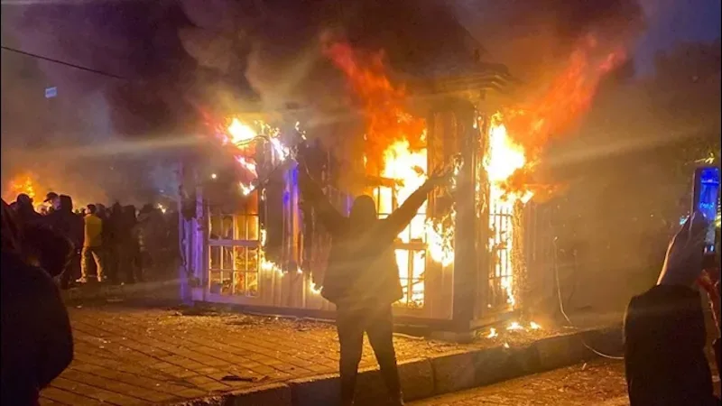 Protestatari în fața unei clădiri în flăcări, simbolizând tensiuni în Iran.