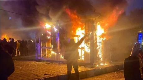 Protestatari în fața unei clădiri în flăcări, simbolizând tensiuni în Iran.