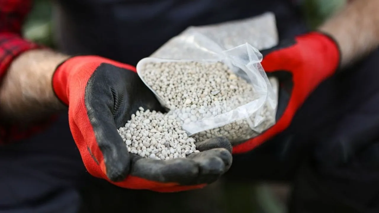 Fermier cu îngrășăminte în mână, evidențiind provocările din agricultură.