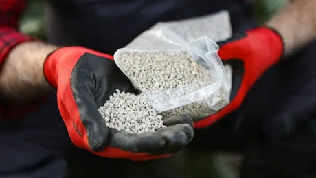 Fermier cu îngrășăminte în mână, evidențiind provocările din agricultură.