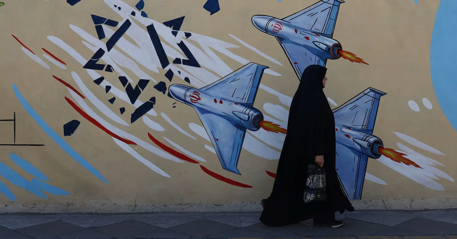 O femeie trece pe lângă un mural cu avioane de luptă în Teheran.