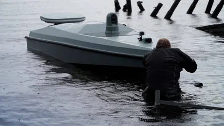 Dronă navală găsită în apă, cu un bărbat inspectând-o.
