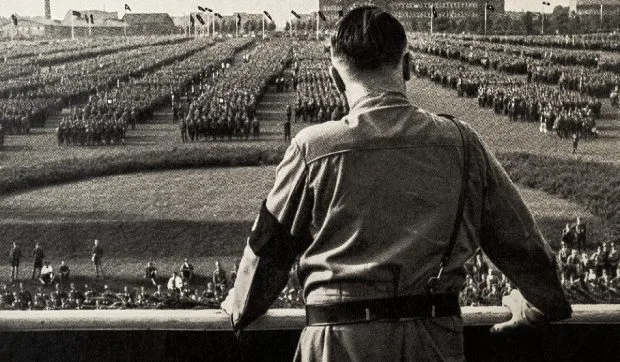 Un bărbat privind spre o mulțime în uniformă, într-un context istoric semnificativ.