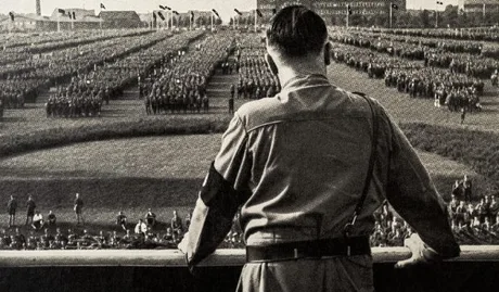 Un bărbat privind spre o mulțime în uniformă, într-un context istoric semnificativ.