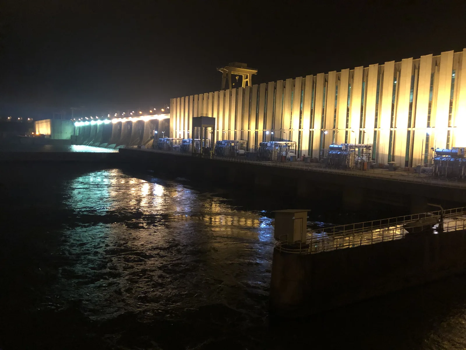 Hidroelectrica la noapte, iluminată, reflectând în apă.