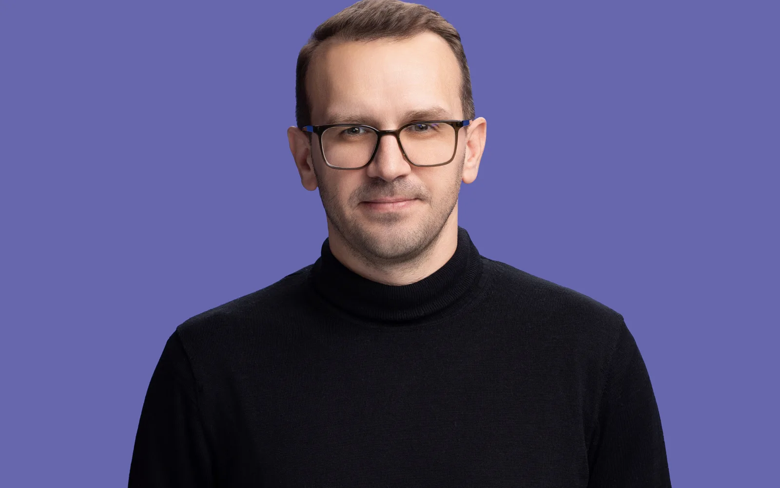 Portret al unui bărbat cu ochelari, îmbrăcat în negru pe fundal violet.