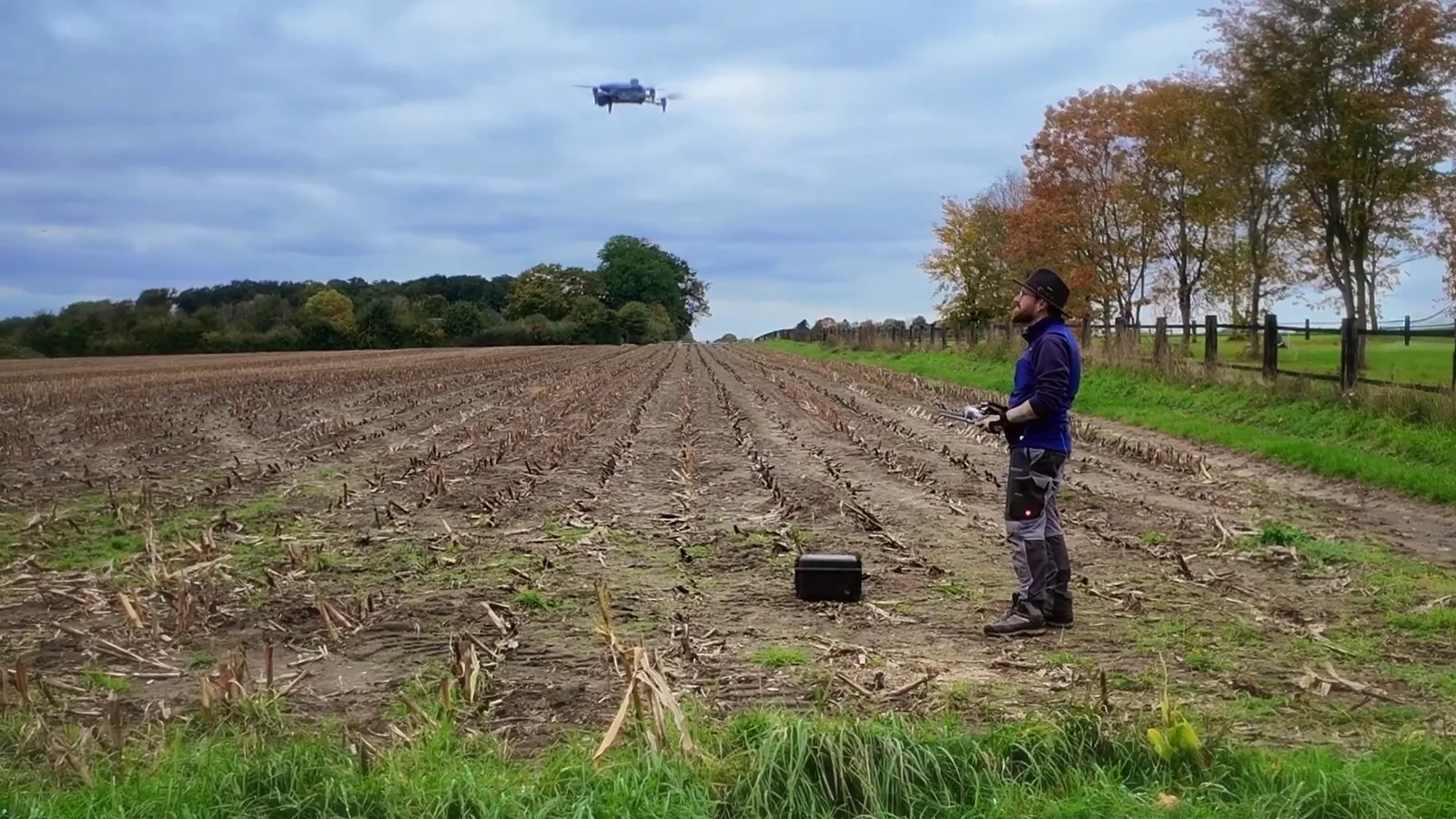 Fermier operând o dronă pe un câmp agricol vast.