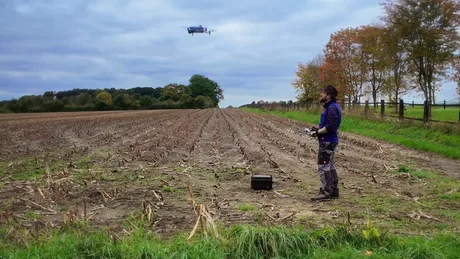 Fermier operând o dronă pe un câmp agricol vast.