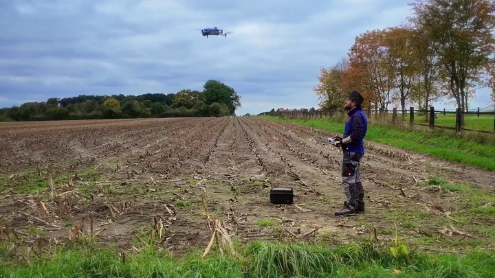 Fermier operând o dronă pe un câmp agricol vast.