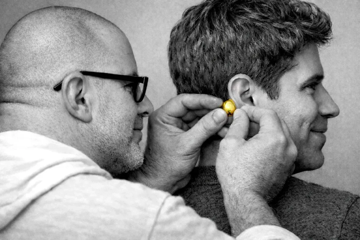 Un bărbat testează o cască wireless pe altcineva, evidențiind designul inedit.